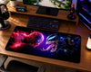 A large gaming desk mat featuring a dramatic Spider-Man and Venom face-off design, shown on a wooden desk alongside a keyboard, mouse, headphones, and monitor.