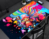 A large rectangular desk mat featuring a colorful cartoon character and swirling rainbow hair design, displayed on a dark gray desk with a chair, plant, and phone nearby.