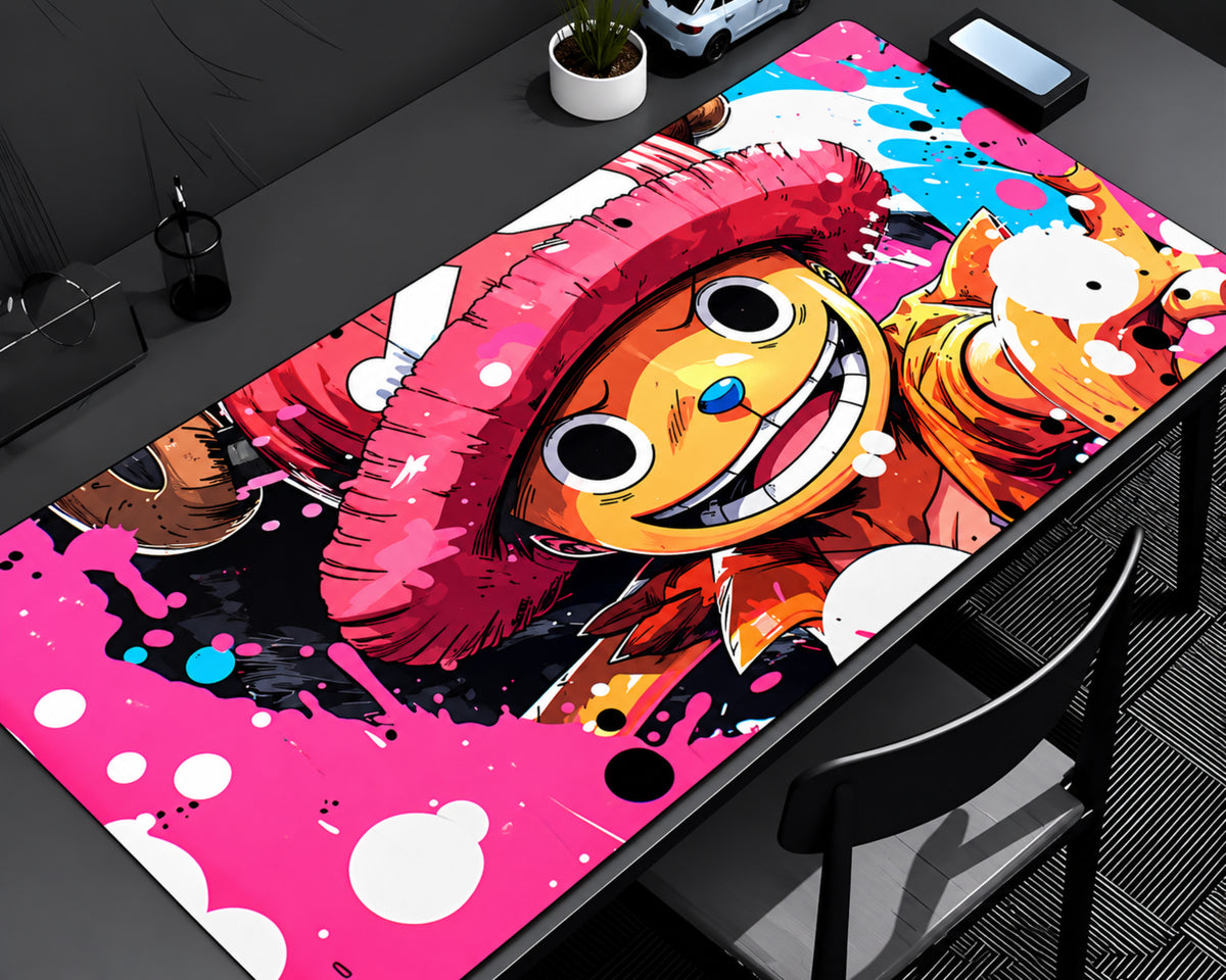 A large rectangular desk mat featuring a colorful anime-style character illustration, shown on a dark desk with a chair, phone, and small plant nearby.