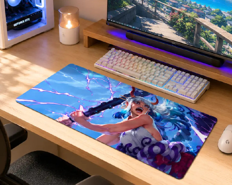 A large rectangular gaming desk mat featuring a colorful anime-style illustration of a female warrior with blue hair and a sword, placed on a light wood desk in front of a keyboard and monitor.