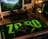A large gaming desk mat featuring a dark green and black design with the word 'ZORD' and a stylized character, displayed on a wooden desk in a gaming setup with a keyboard, mouse, headphones, and monitor.