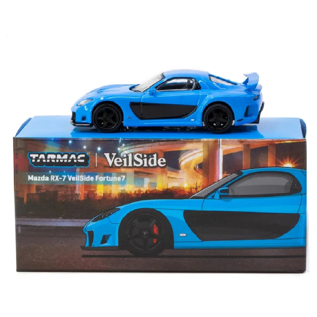 A blue and black Tarmac VeilSide Mazda RX-7 diecast model car displayed on top of its retail box against a white background.