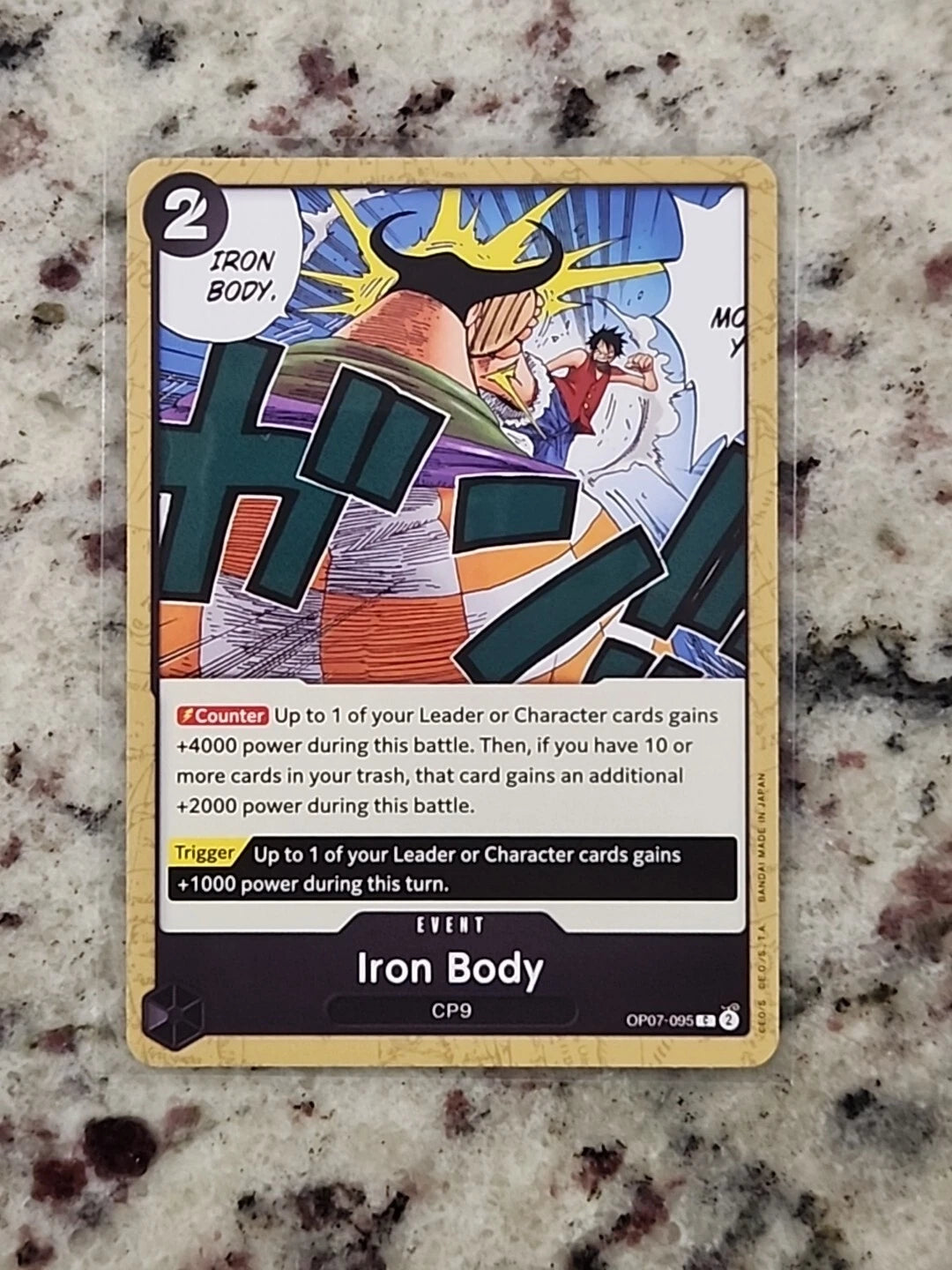One Piece TCG event card OP07-095 titled Iron Body featuring a muscular figure with yellow hair in a defensive stance while Luffy runs in the background.