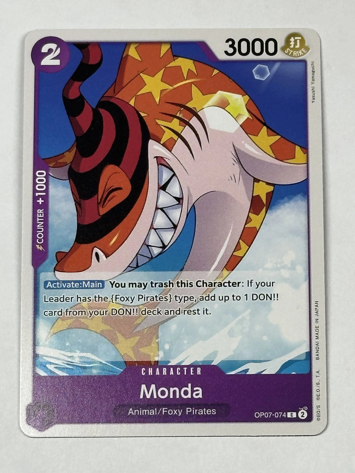 One Piece TCG character card OP07-074 featuring Monda, a large shark with a red and black spiral horn and star patterns on its body, swimming underwater.