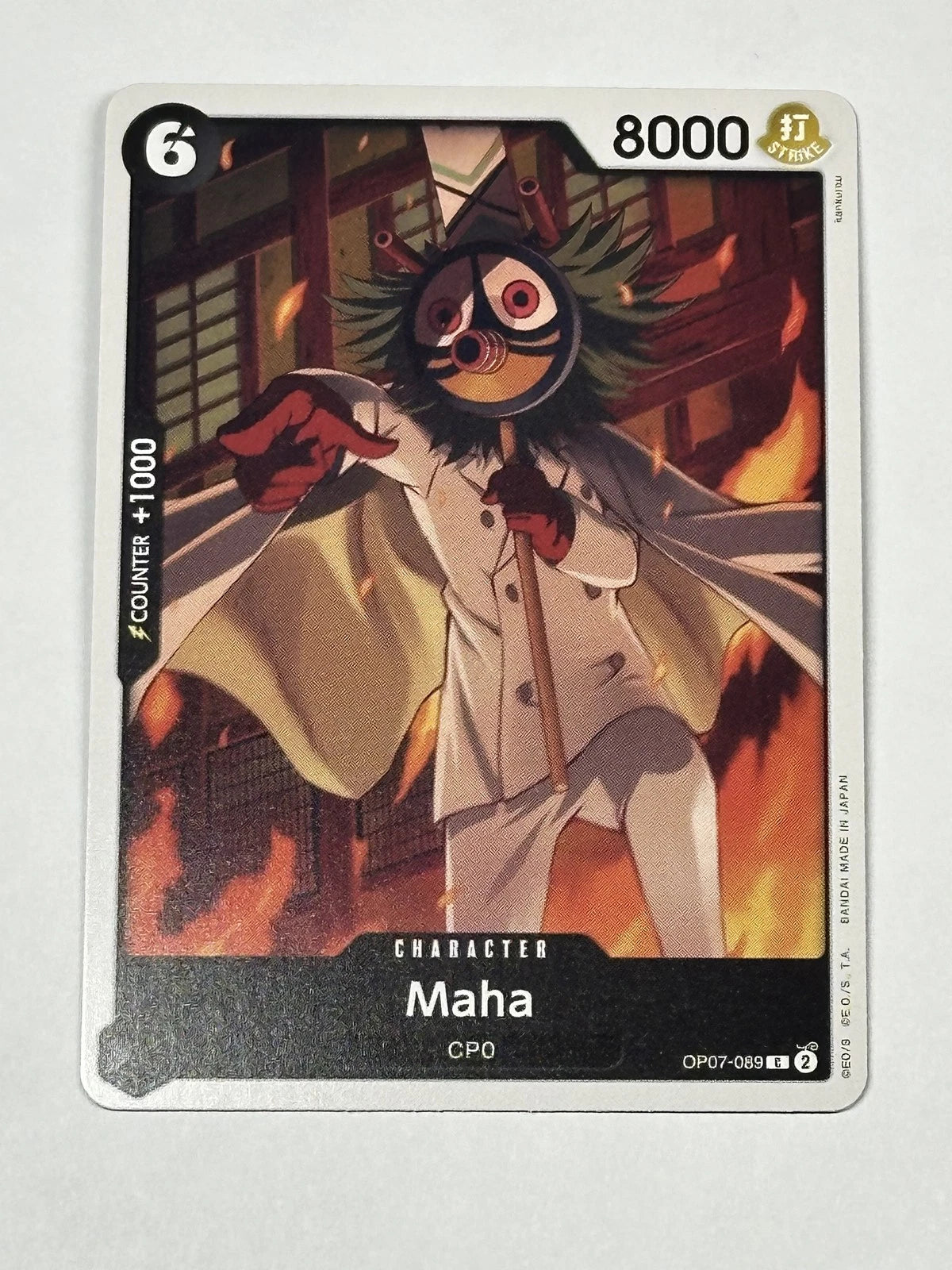 One Piece TCG character card OP07-089 featuring Maha, a CP0 agent in a white suit and a round patterned mask, pointing forward amidst burning flames
