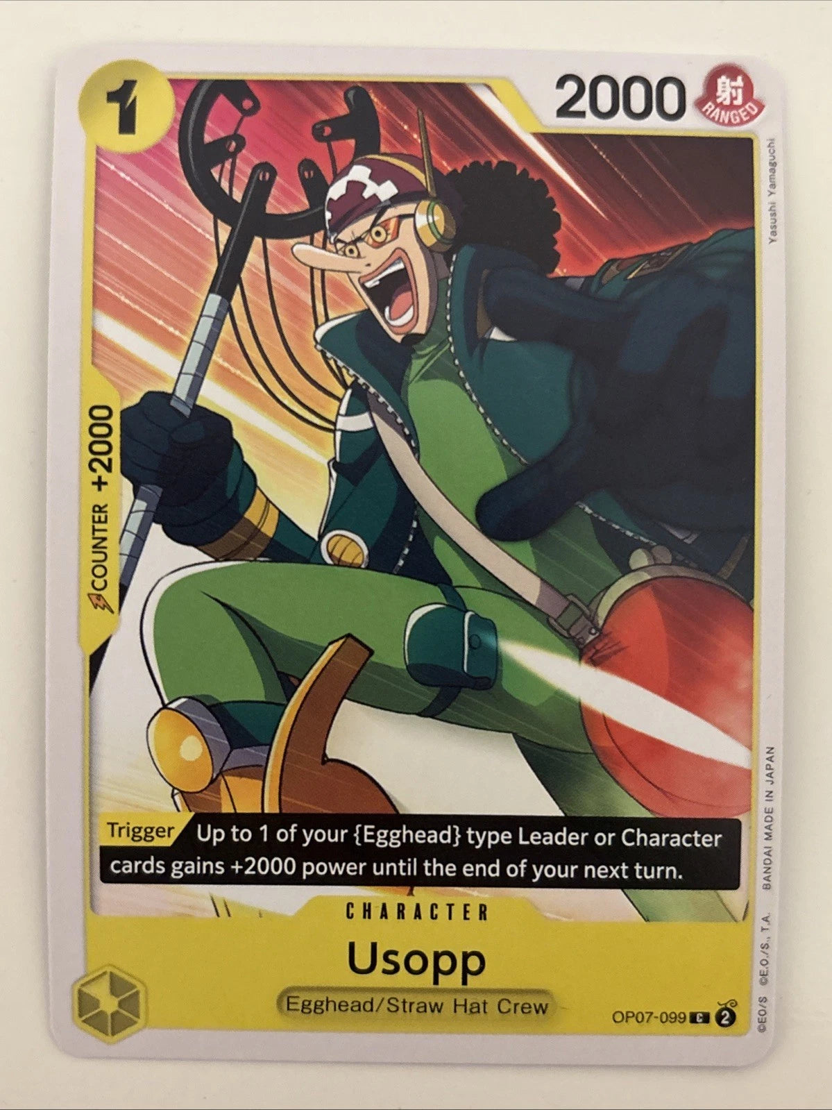 One Piece TCG character card OP07-099 featuring Usopp in a green suit and orange bag, screaming while holding his slingshot against a backdrop of orange and yellow streaks.